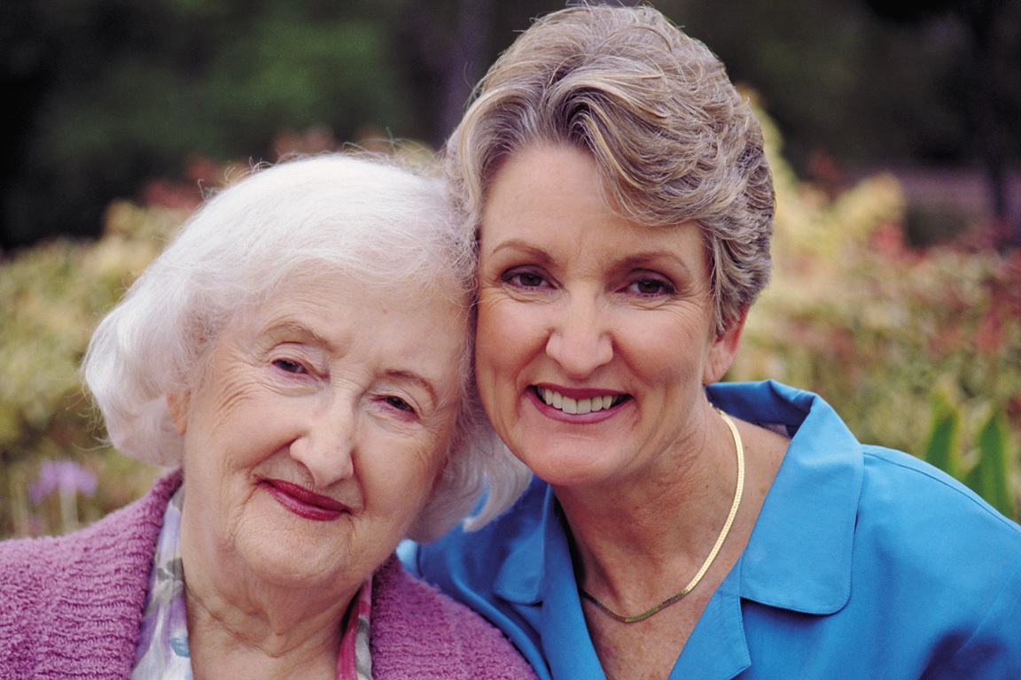 An older woman and a younger woman smile, the older woman leaning on her companion. Learn more about senior home care assistance at Families Choice Home Care.