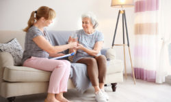 A caregiver sits with an older woman receiving in-home care.