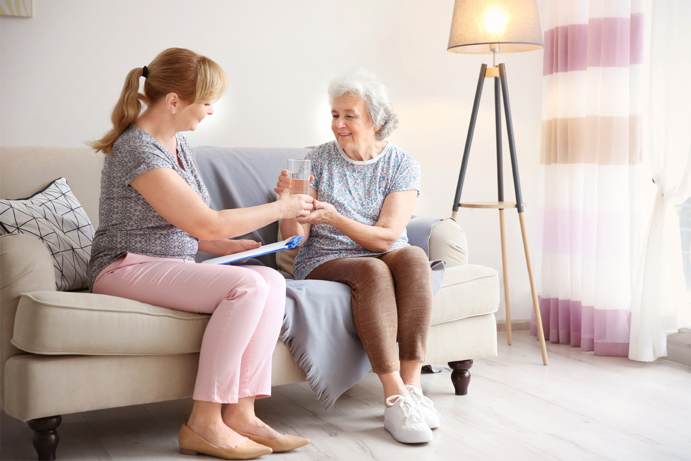 A caregiver sits with an older woman receiving in-home care.