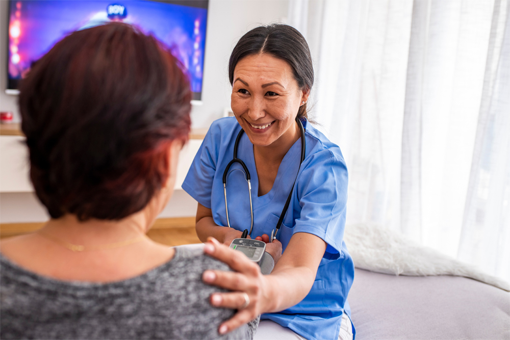 A smiling aide performs a blood pressure check as part of in-home care for a senior with dementia.