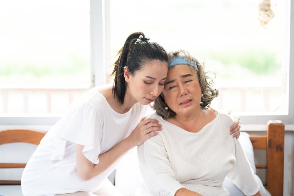 A young Asian woman appears to be suffering from caregiver burnout as she assists her sick, elderly mother.