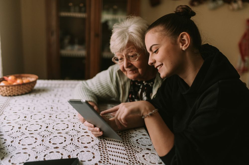 A grandmother and granddaughter do online research on how to get 24-hour care for the elderly at home.