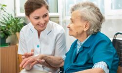 An elderly woman who arranged for in-home palliative care is assisted by an aide with hygiene care.