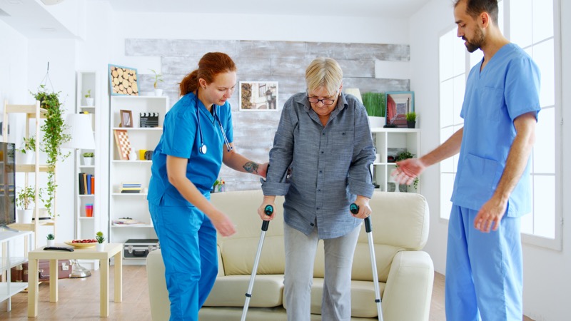 A caregiver helps her female senior client take a walk as part of the post-hospital in-home care after knee surgery.