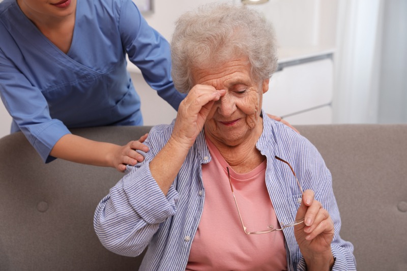 An elderly woman with Alzheimer's rubs her head in confusion as an aide tries to comfort her.