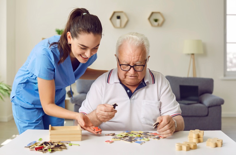  An in-home caregiver helping a dementia patient put together a jigsaw puzzle to stimulate their brain.