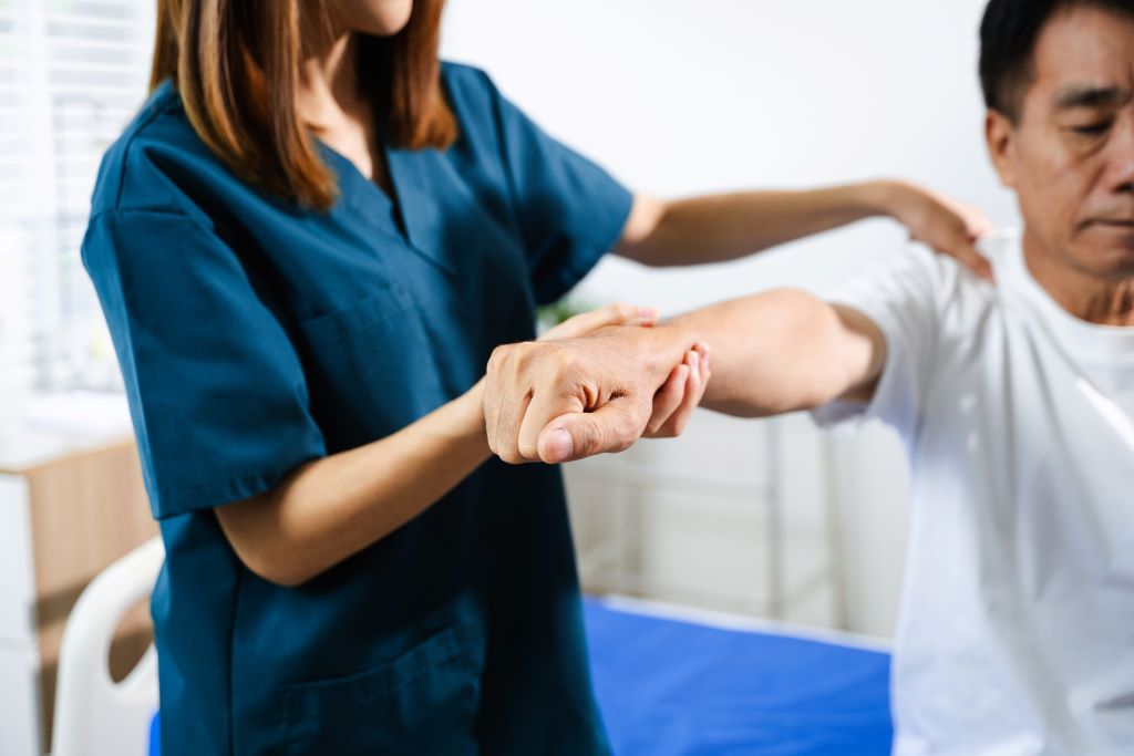 A caregiver guides a male stroke survivor with gentle exercise during his recovery.