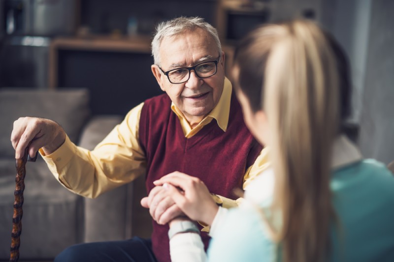 A caregiver sits with a smiling senior man.