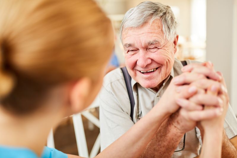 A smiling senior chats with his caregiver at home.