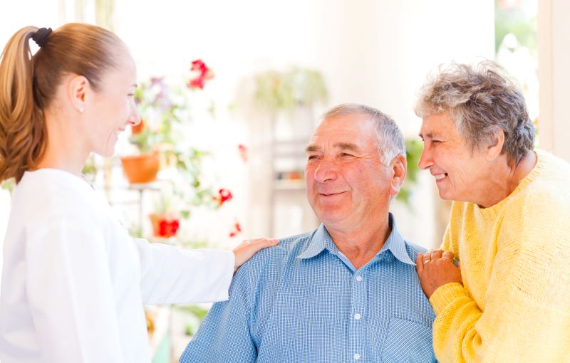 A senior couple smiles at their in-home caregiver.