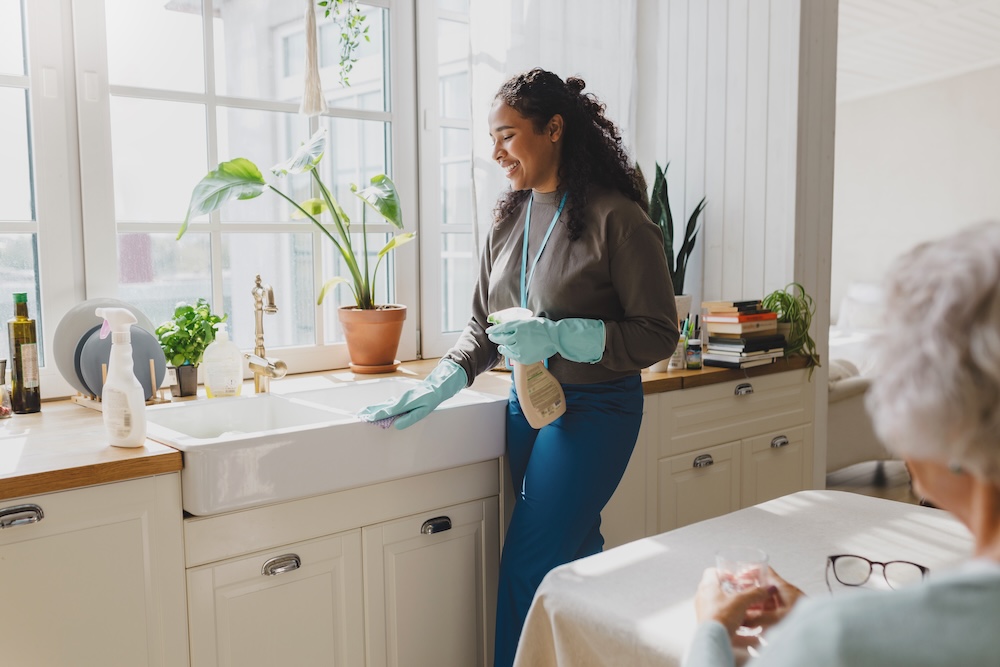 A senior watches on as her caregiver provides home cleaning support.