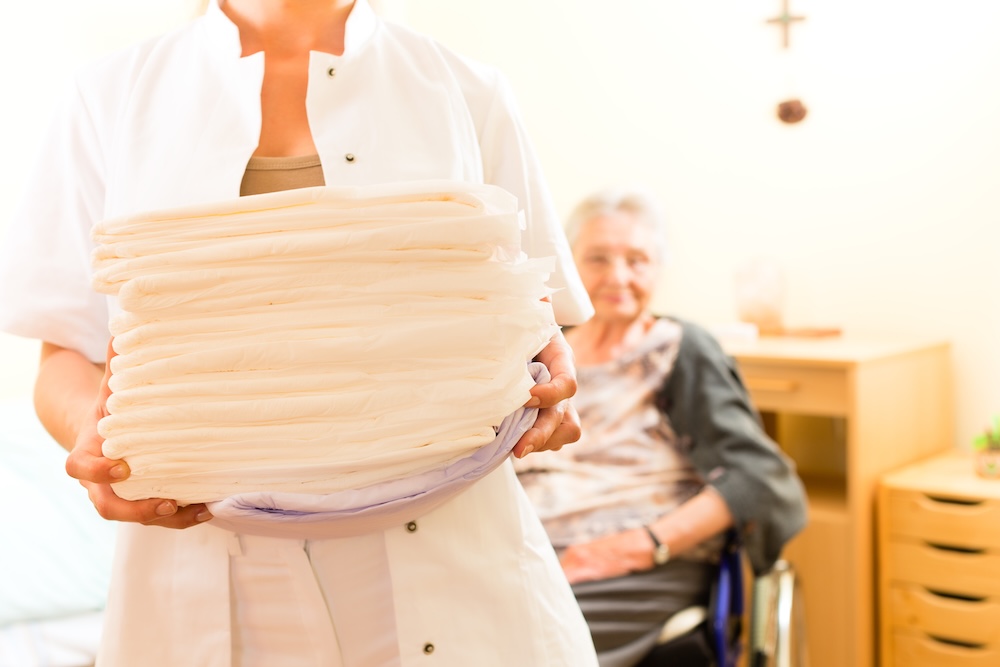 Caregiver holding fresh linens for elderly woman during senior housekeeping services visit