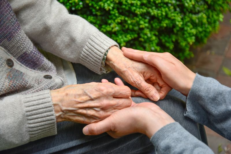 Caregiver holding hands with elderly woman.
