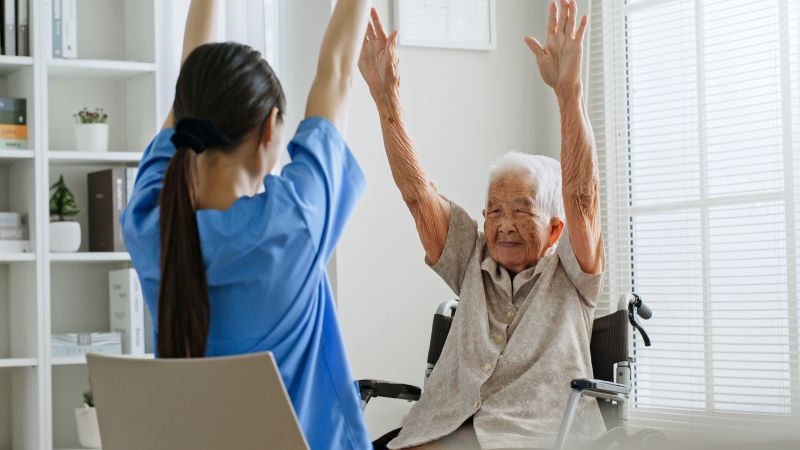 Caregiver and elderly woman doing physical therapy.